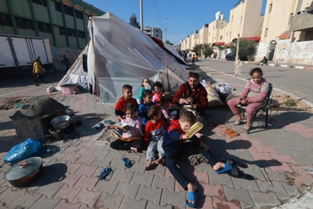 Uma família palestina sentada na rua em frente a uma tenda rústica feita de lona