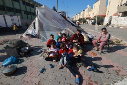 A Palestinian family sits on the street outside a rough tent made of tarpaulin