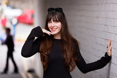 A woman in a black jumper with long dark hair standing next to a wall