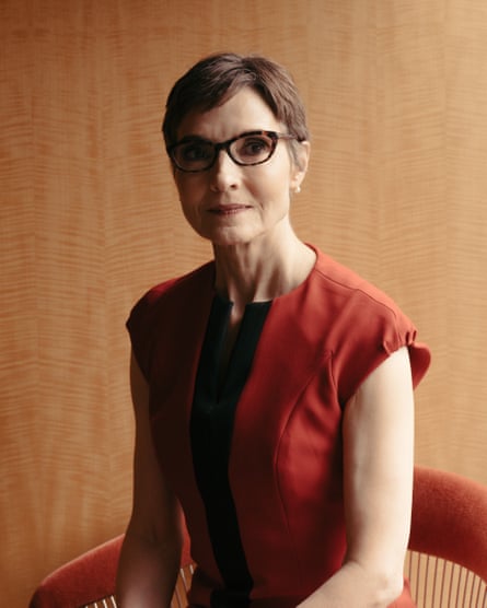portrait of a woman with short hair, glasses, in a red dress against a beige wall