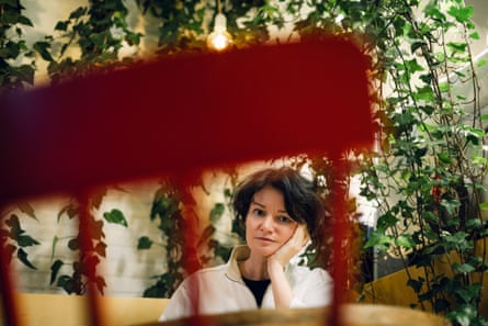 A glum-looking woman sitting at a table with a climbing plant behind her
