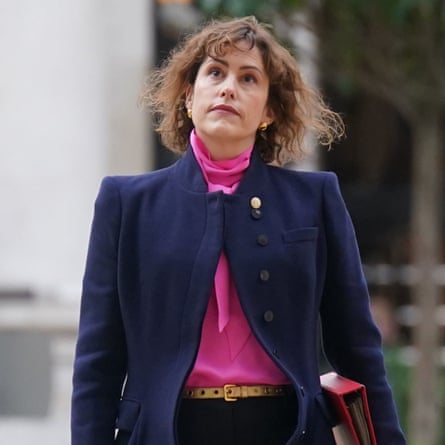 Victoria Atkins, in a shirt with a scarf under her jacket, walks along holding a binder