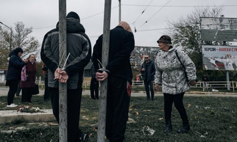 Local residents look at two alleged collaborators tied by the hands to pillars in Kherson.