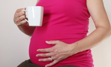 pregnant woman with mug in hand holding her stomach