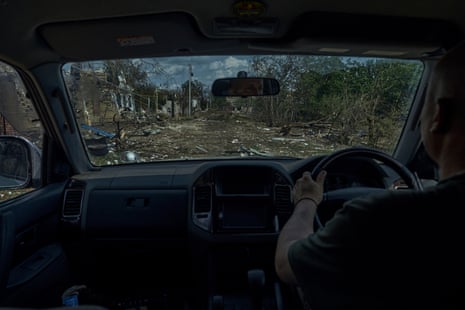 A man drives through the village of Kozatske, strewn with debris after flooding and shelling.