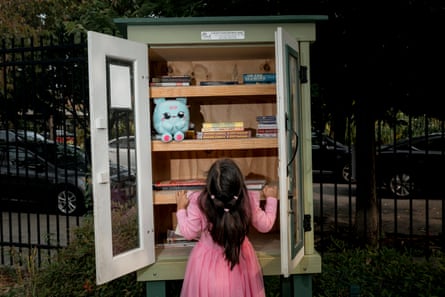 A girl opens an outdoor bookcase while the toy sits on a shelf