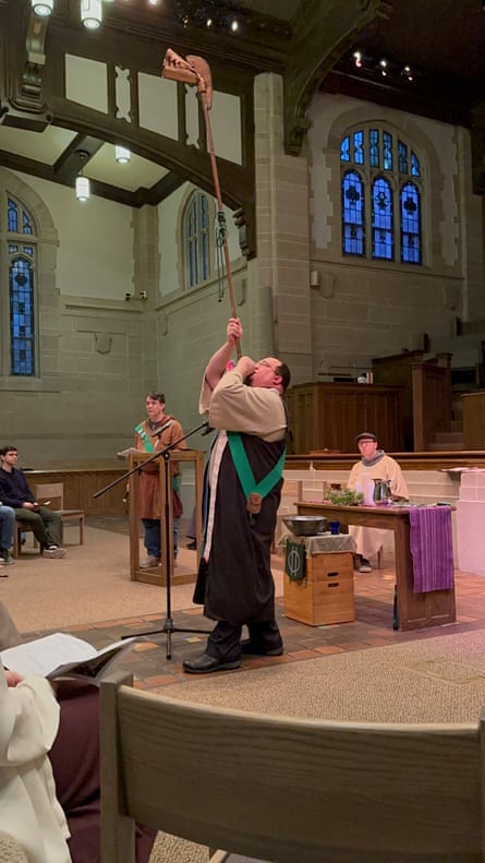 Person in large stone chapel holding very long wooden or straw ... horn? and looking or blowing upward.