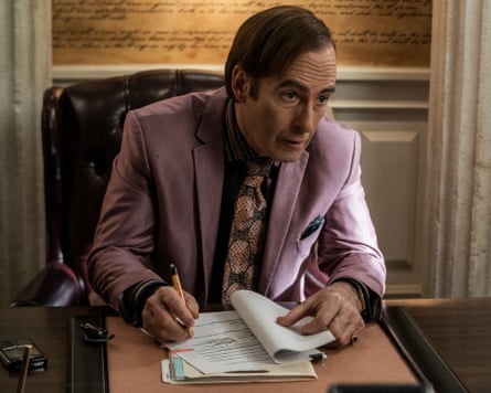 A lowlife-looking lawyer in a pink suit and loud tie signs papers at a desk