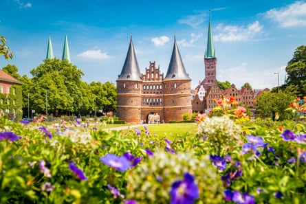 A red brick gate with pointy spires with a flowerbed in the foreground.