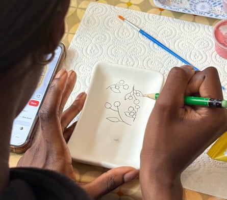 Closeup of a woman's hands as she holds and paints a pattern on a white pottery dish.