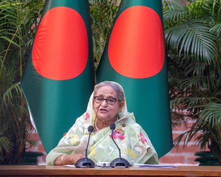 Sheikh Hasina sits in front of two Bangladesh flags