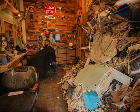 A barber cuts a client's hair in his damaged shop, Beirut