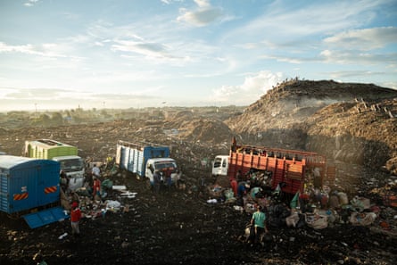 Four trucks in a rubbish-strewn landscape next to a large mound of rubbish
