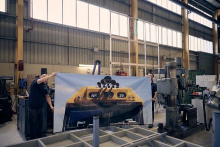 Two men in a large shed holding a large poster showing the top of a train
