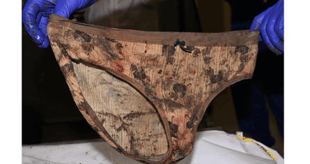 A pair of women’s pants, with unspecified dirty marks, held up by gloved hands as evidence.