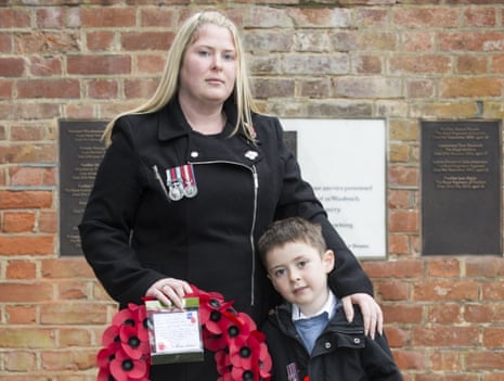Rebecca Rigby wearing a soldier's medals and holding a poppy wreath standing with her arm round a young boy