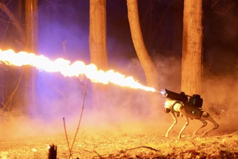 a stream of fire erupts from a flamethrower atop a robot dog in what appears to be a wooded area, which is in no way concerning at all