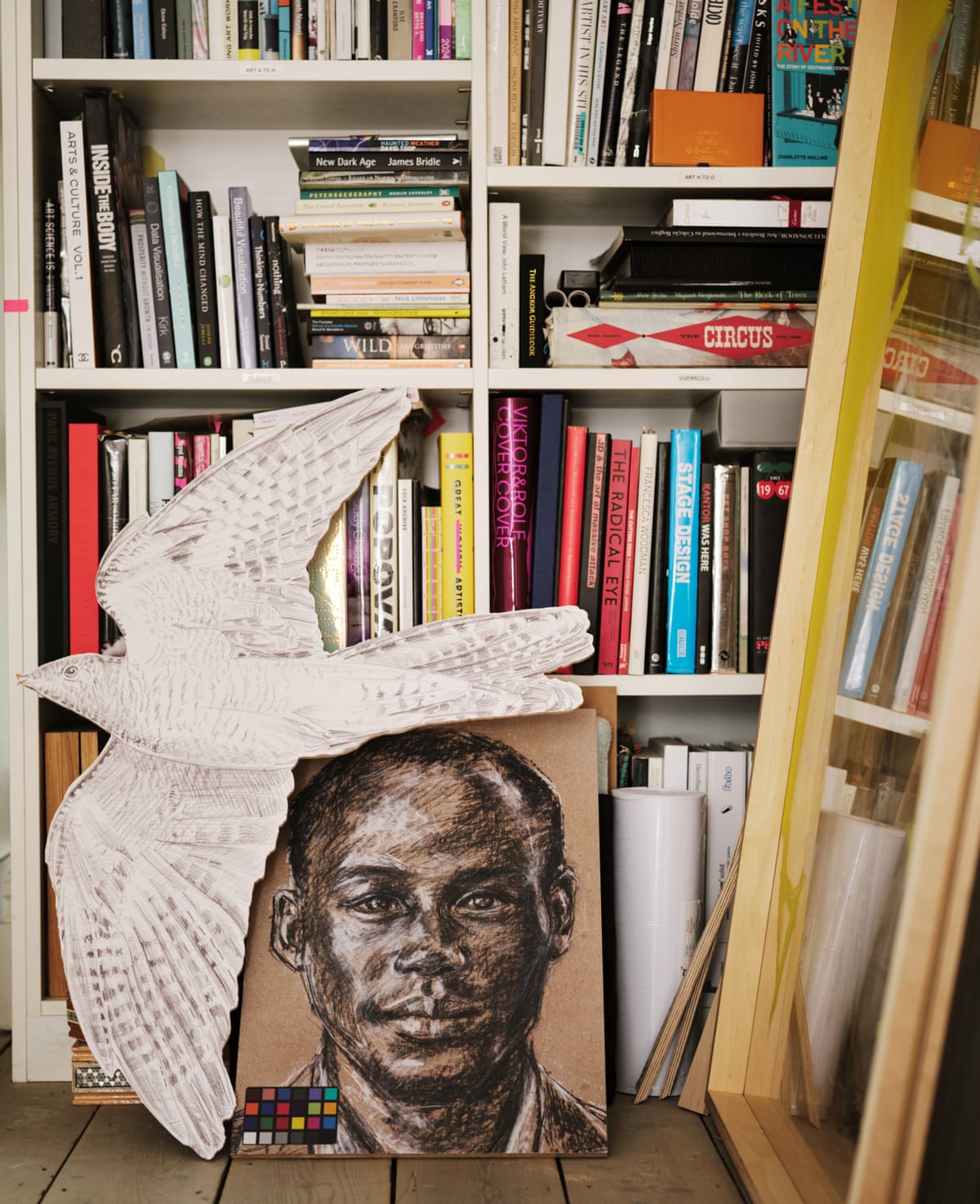 A bookcase with a painting of a man and a cutout of a bird on the floor