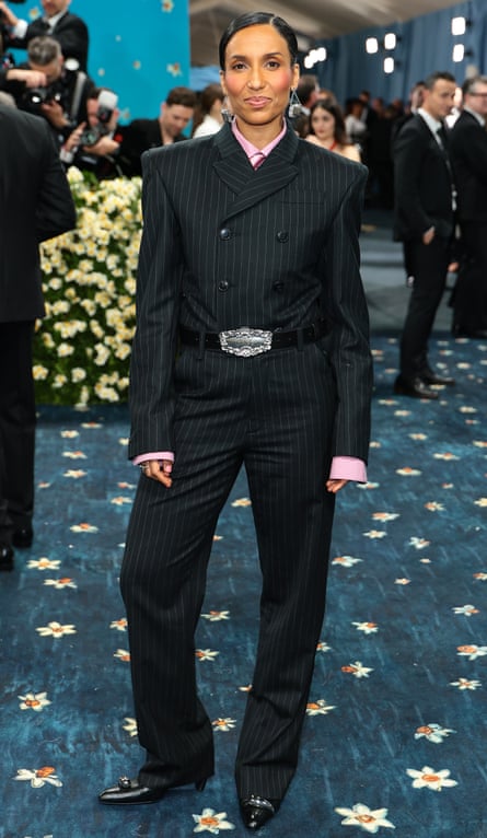 Chioma Nnadi in a black pinstripe suit with a black belt with elaborate silver buckle and silver handbag-shaped earrings
