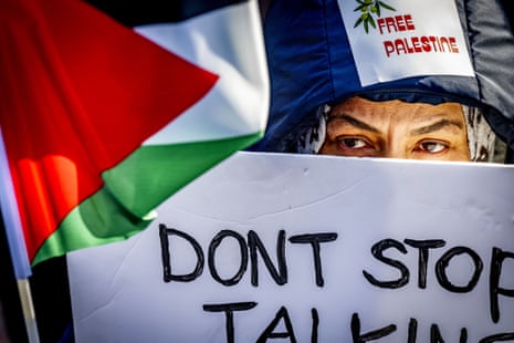 a person holds a Palestinian flag and a sign that reads "free Palestine"