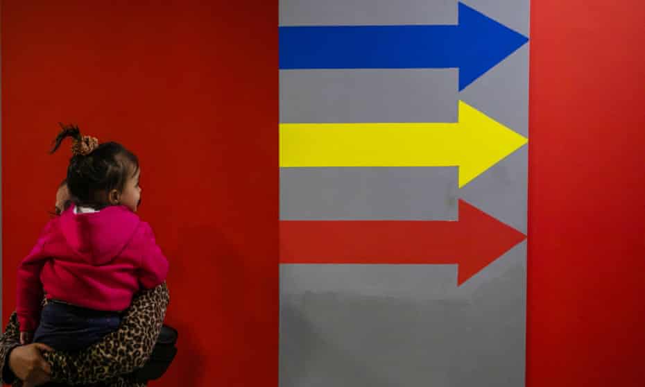 A child sits on an adult's shoulders against a backdrop of a wall painted with arrows