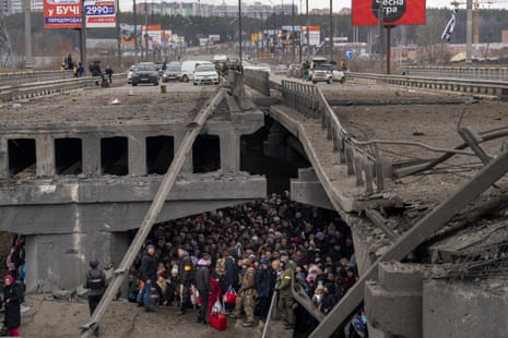 People crowd under a destroyed bridge with vehicles above