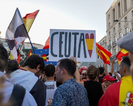 Crowd of people raising flags of Spain and the Spanish enclave of Ceuta and a placard reading ‘Ceuta’ featuring a red and yellow heart.