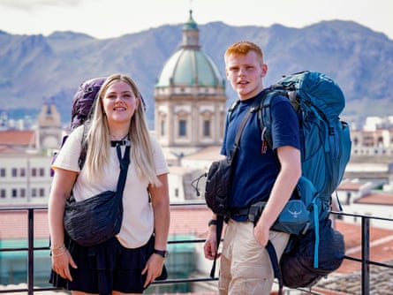 A young woman and man wearing rucksacks stand on a balcony