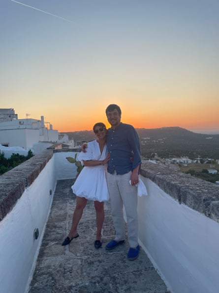 Man and woman standing in front of sun setting behind hills