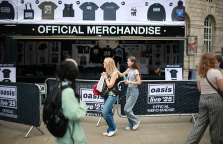 People walking past an Oasis ‘official merchandise’ stall with items for sale including T-shirts, hoodies and tote bags