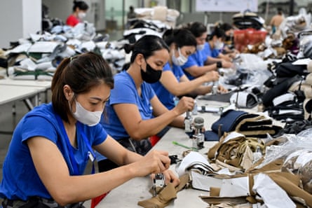 Row of workers stretching away from the camera, wearing face masks and blue shirts, seated at tables working on piles of fabric