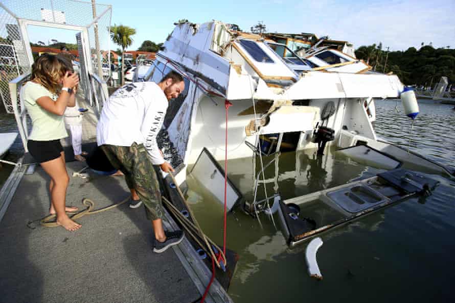 A couple look at a damaged boat in a marina at Tutukaka, New Zealand, Sunday, Jan. 16, 2022, after waves from a volcano eruption swept into the marina.
