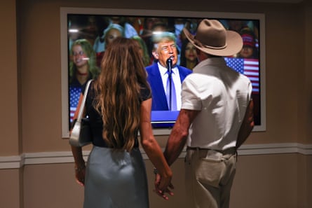 A couple watches Trump speak on a screen at the convention centre.