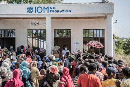 A crowd of people gather outside a building that says IOM UN Migration on it