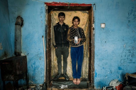 A young man and woman stand in a doorway. The woman is holding a mobile phone