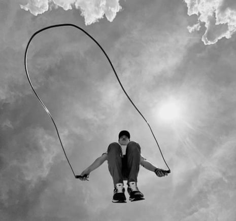 A black and white image of a man jumping with a skipping rope, shot from below, with clouds above