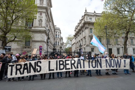 People at a protest waving a transgender flag and holding a banner that reads ‘Trans liberation now!’