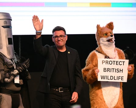 Burnham waves to the crowd standing next to a man dressed in a fox costume.