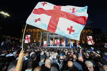 Large group of middle aged people in front of stage with Georgian flags being waved