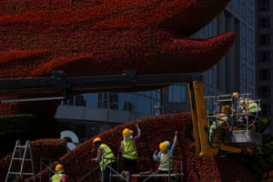 Workers wearing hard hats use a crane to help them place flowers into a large structure
