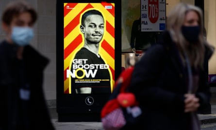 Pedestrians walk past an electronic billboard promoting the NHS’s Covid vaccine booster programme, in central London, in December 2021.