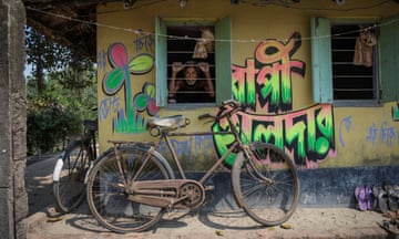 A man looks through the window of a property which has the slogan and logo of a political party painted on it and a bicycle resting against it