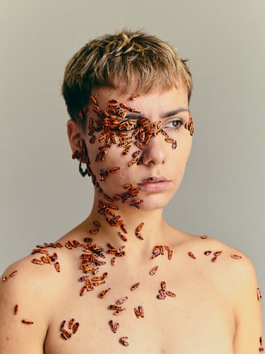 A woman whose face and bare shoulders are covered with red-winged beetles
