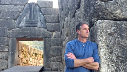 A man in a blue top, with stone walls behind him