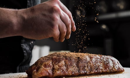 The hand of a male chef puts salt and spices on a raw piece of meat.