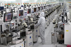 A technician in a white hazmat suit before a row of about 20 identical looking machines