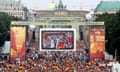 A big crowd of German football fans wave German flags in front of a giant screen in front of the Brandenburg Gate
