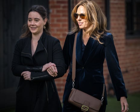 Jennifer Keyte, a woman with wavy, shiny hair and sunglasses, walks on the arm of another woman.