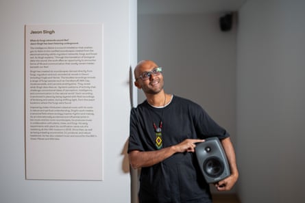 Jason Singh holding a speaker and leaning against an exhibit sign