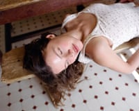 A woman lying on a wooden bench wearing a vest with a floral pattern